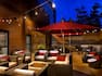Tables With Red Umbrellas, Chairs, and Fire Pit Under Illuminated String Lights on Hotel Exterior Patio at Night
