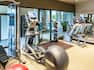 Fitness Center With Red Exercise Ball, Weight Machine, Bench, Cardio Equipment, Glass Entry Door, Weight Balls, and Large Mirror