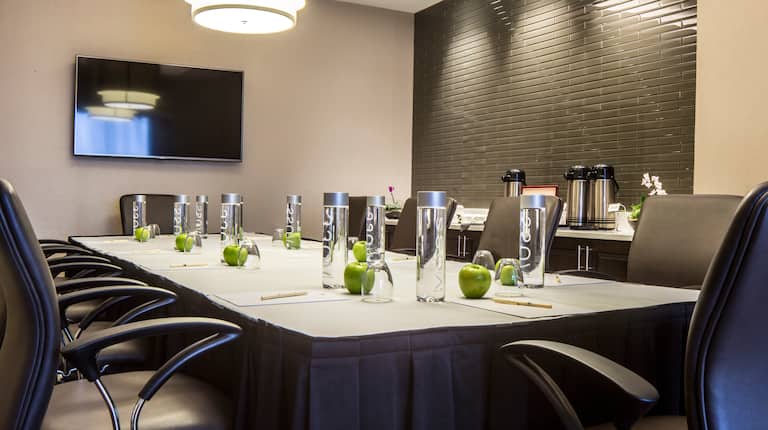 TV, Refreshment Center, Black Chairs, Water Bottles and Green Apples on Table in a Boardroom