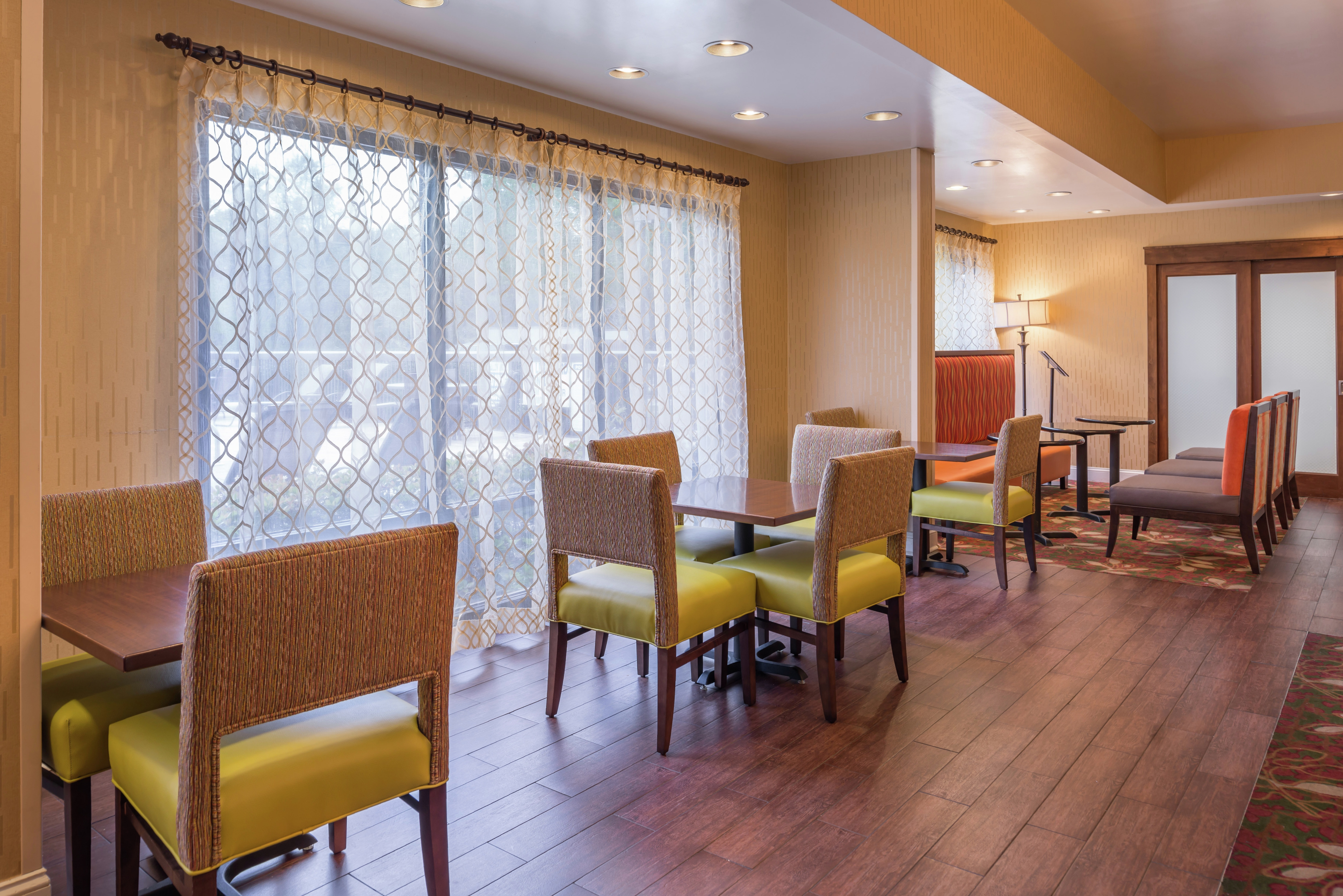 Tables, Chairs, Booths, and LArge Windows With Sheer Drapes in Hotel Dining Area
