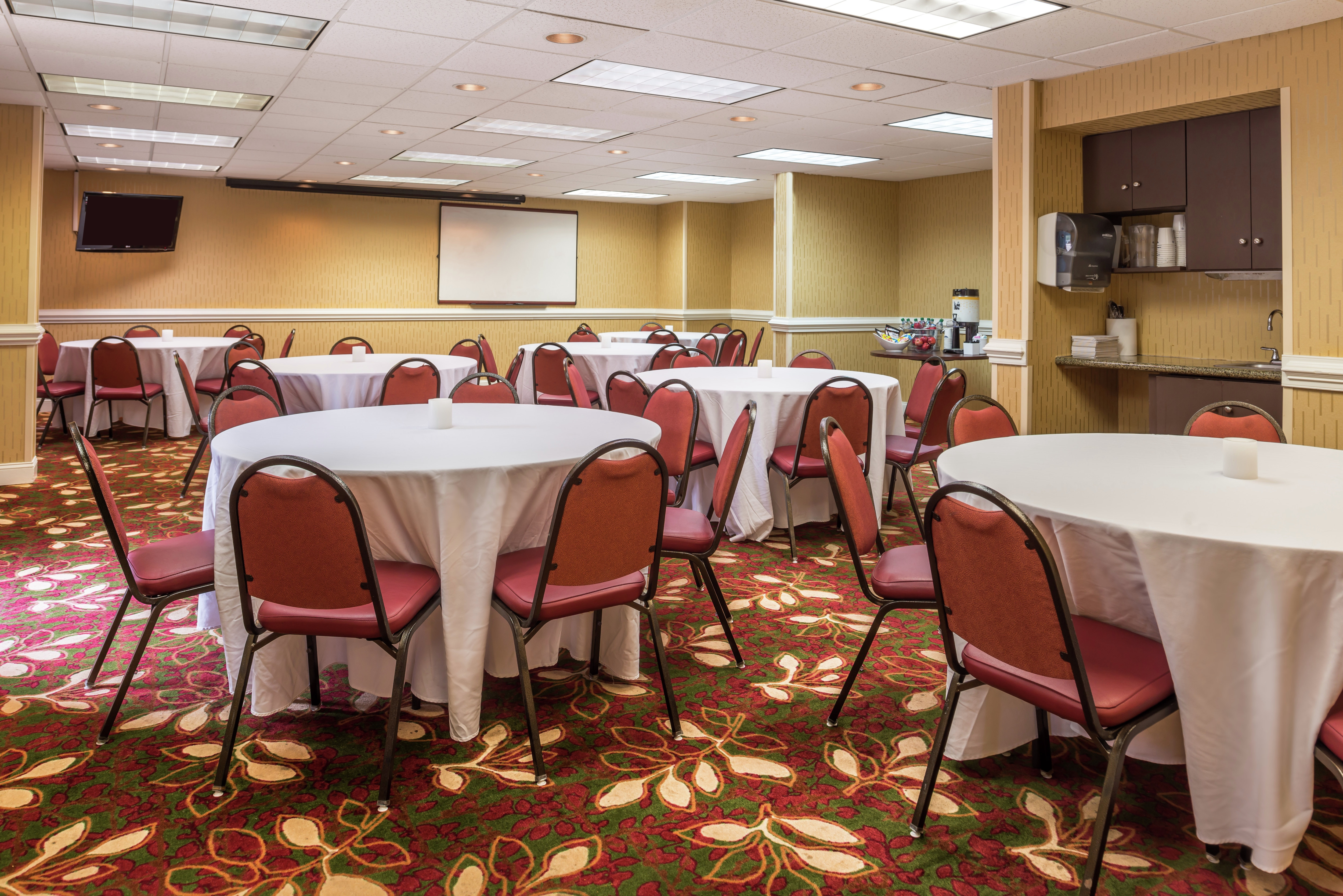 Red Chairs at Banquet Tables With White Linens, TV, Presentation Screen, and Refreshment Area in Meeting Room