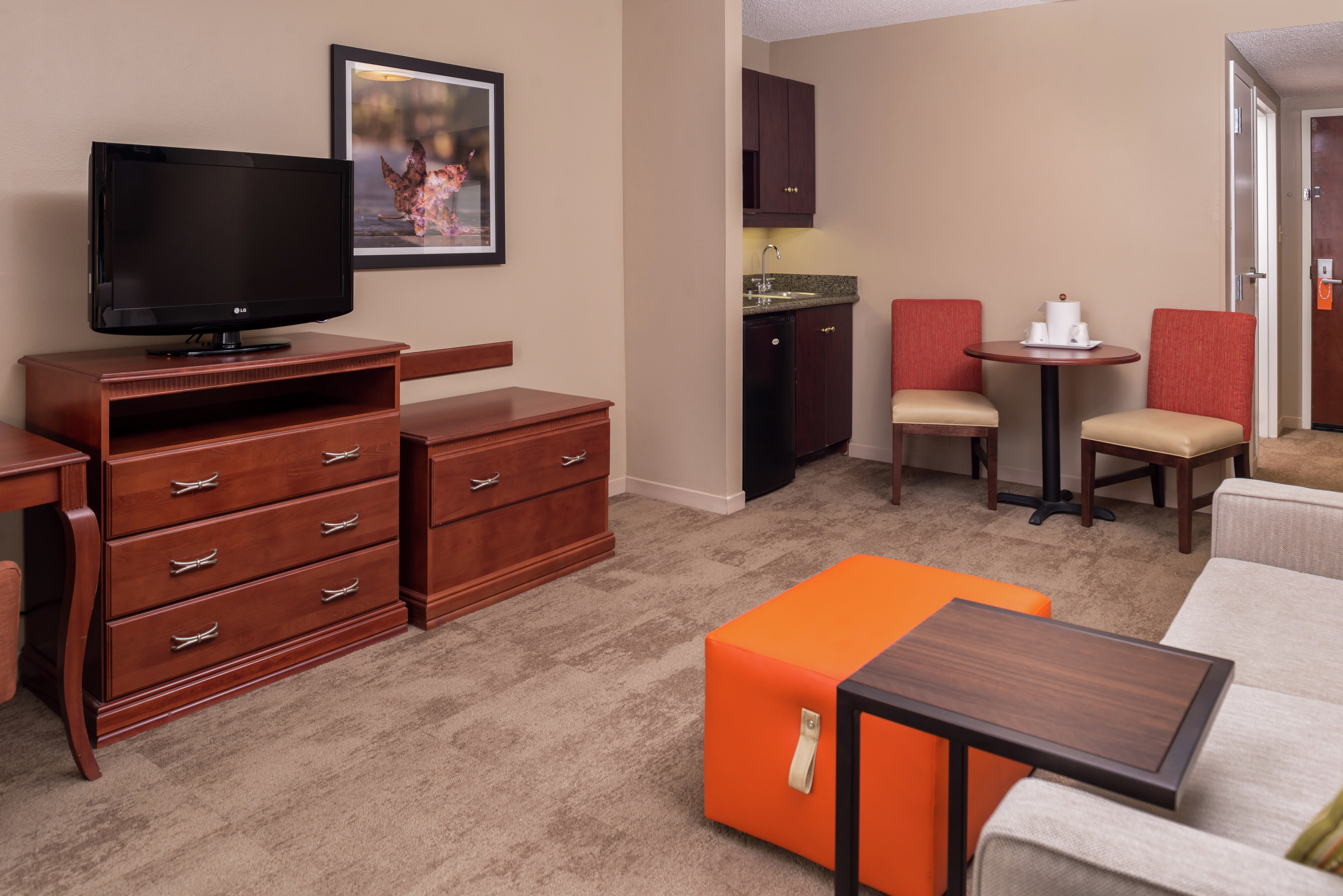 Sofa Bed, Orange Ottoman, TV, Wet Bar, Seating for Two at Dining Table, and Entry in Deluxe Living Room