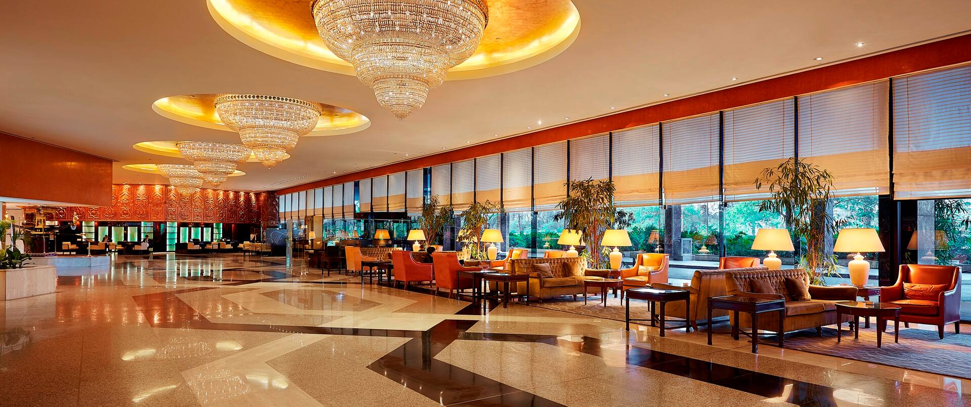 Hotel lobby with sofas, soft chairs, coffee tables, and floor-to-ceiling windows with outdoor view