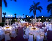 Patio by palm trees at night with white banquet candlelit tables