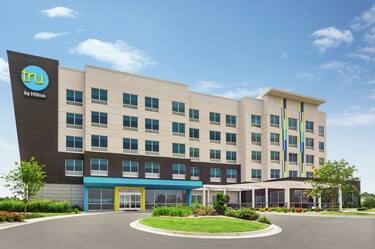 Modern Tru hotel exterior featuring lush landscaping, outdoor patio, and bright blue sky.