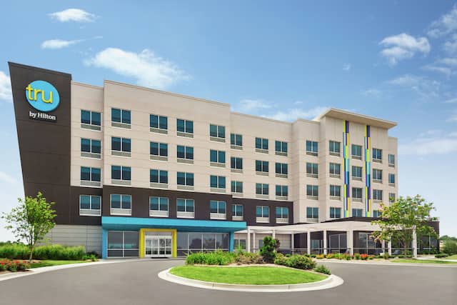 Modern Tru hotel exterior featuring lush landscaping, outdoor patio, and bright blue sky.