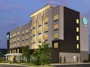 Modern Tru hotel exterior featuring lush landscaping, glowing guestroom windows, and dusk sky.