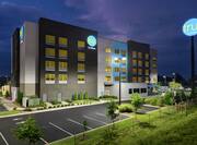 Modern Tru hotel exterior featuring lush landscaping, glowing guestroom windows, and dusk sky.