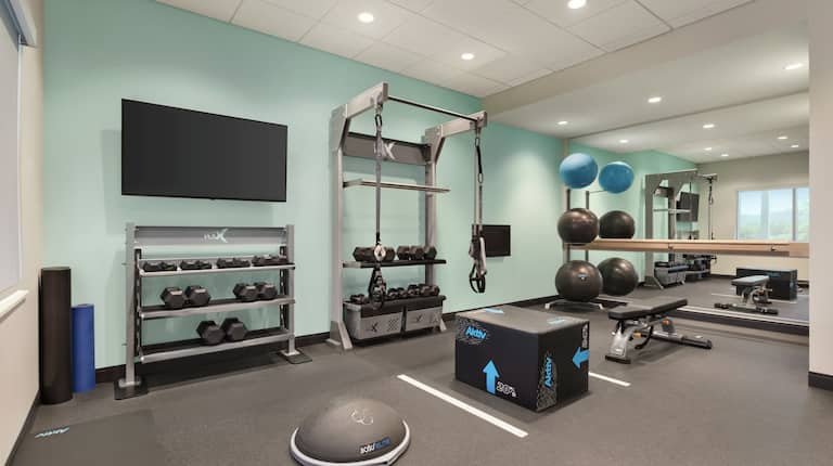 Convenient on-site fitness center featuring free weights, TV, benches, and mirrored walls.