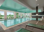 Spacious indoor pool featuring large floor to ceiling windows, ample lounge seating, and accessible chair lift.