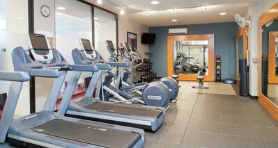 Fitness Center With Cardio Equipment, TV, Free Weights, Large Mirrors, Weight Bench, Weight Balls, and Water Cooler