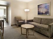 Bright living area in suite featuring sofa, dining table, and view into private bedroom with two double beds.