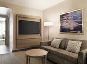 Lounge area in suite featuring sofa, coffee table, TV, and view into private bedroom.