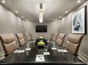 Large boardroom table in meeting room featuring stationary supplies, ergonomic chairs, and TV.