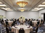Ballroom with about 10 round cloth-covered tables with place settings and 8 chairs each