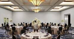Ballroom with about 10 round cloth-covered tables with place settings and 8 chairs each