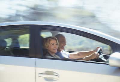 Older couple driving in a white car