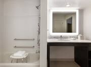 Bright accessible bathroom featuring tub with seat, grab bars, and large vanity.