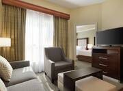 Spacious lounge area in two bedroom accessible suite featuring comfortable seating, TV, and view into private bedroom.