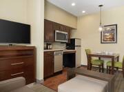 Spacious living area in two bedroom accessible suite featuring lounge area with TV, fully equipped kitchen, and dining table.