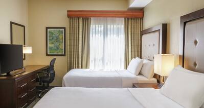 Bright private guestroom in two bedroom accessible suite featuring comfortable beds, TV, and work desk.