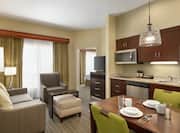 Spacious living area in one bedroom suite featuring fully equipped kitchen, dining table, and lounge area with TV.