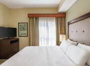 Bright private bedroom in one bedroom suite featuring comfortable king bed, dresser, and TV.