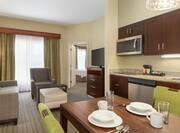 Spacious living area in one bedroom suite featuring fully equipped kitchen, dining table, and lounge area with TV.