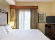 Bright private bedroom in two bedroom suite featuring comfortable king bed, dresser, and TV.