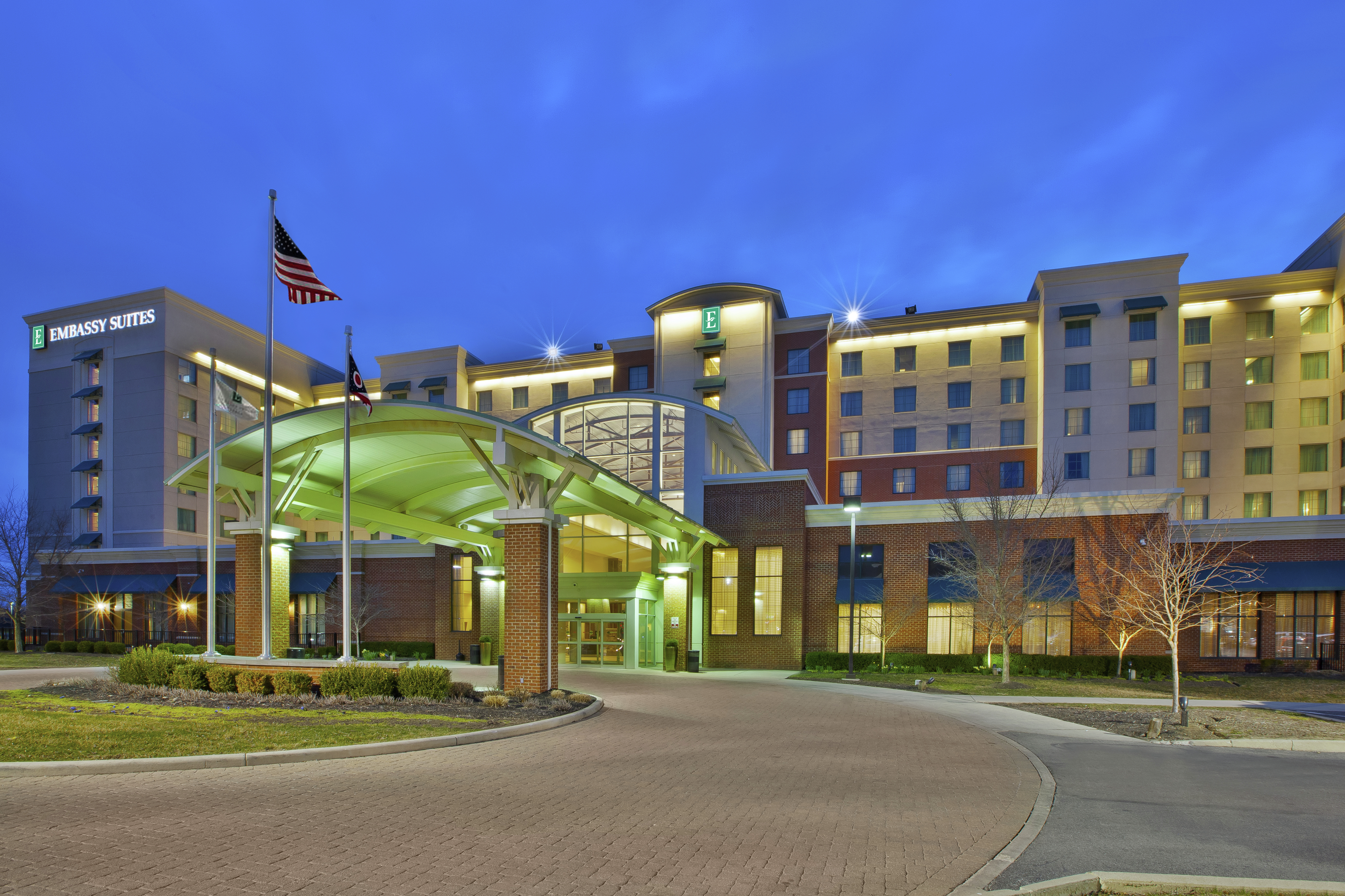 Illuminated Hotel Exterior, Porte Cochère, Flagpoles, and Landscaping at Dusk