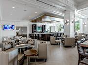 Hotel social space with bar, soft chairs, dining tables and chairs, TV, and floor-to-ceiling windows with outdoor view