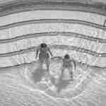 Fotografie cu un bărbat și o femeie în piscină, realizată de sus 