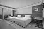 Hotel room with two double beds, orange headboard, work desk, and windows showing a city outside.