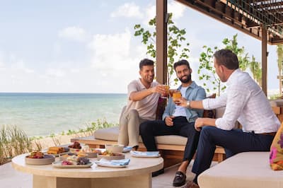 Three men toast drinks by the ocean
