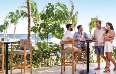 Four people share drinks and food by the ocean
