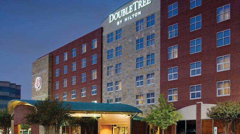 Angled View of Illuminated Hotel Exterior With Signage, Entrance, Landscaping at Night