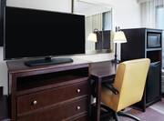 Close Up of Work Desk with Illuminated Desk Lamp, Chair, Flat Screen TV, Microwave, and Mini-Fridge in Guest Room