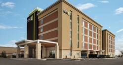 Modern Home2 Suites hotel exterior featuring porte cochere and bright blue sky.