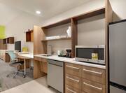 Spacious accessible studio suite featuring fully equipped kitchen, work desk with ergonomic chair, and TV.