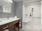Spacious accessible bathroom featuring roll in shower with seat, mobile shower head, and vanity.