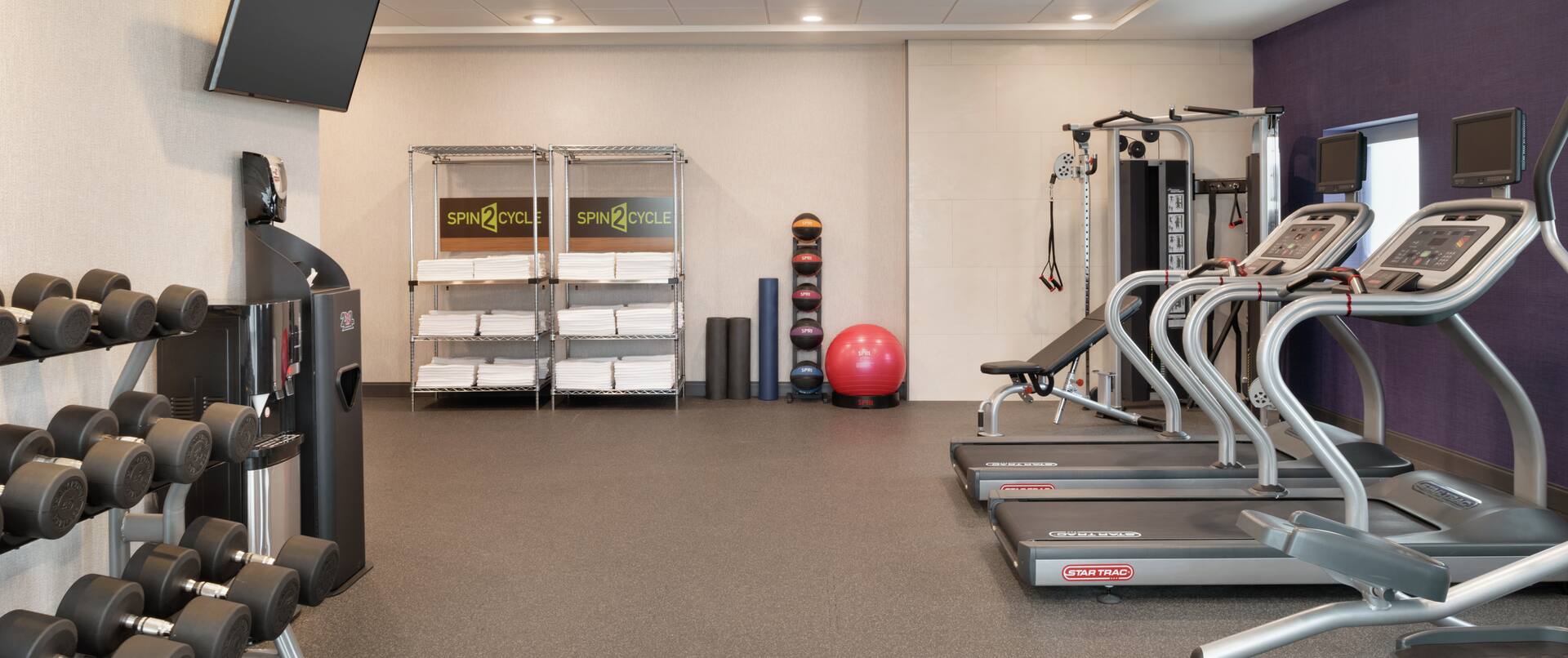 Spacious fitness center featuring cardio machines, free weights, TV, and complimentary towels.