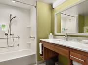 Spacious accessible bathroom featuring tub, mobile shower head, vanity, and mirror.