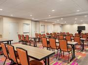Bright meeting room featuring classroom style tables and chairs, TV, and podium at front of room.