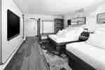 Modern guest room with two beds, TV wall display, desk, mirror, and open closet.
