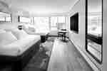Modern hotel room with two beds, windows, chair, table, and wall-mounted TV.