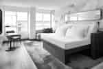 Modern guest room with a bed, chair, small table, sofa, large windows, and mirror.