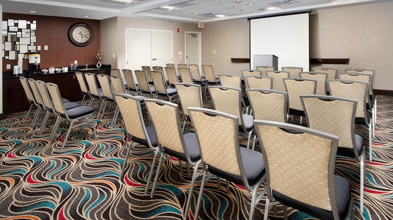 Meeting Space Arranged Theater Style With Rows of Chairs Facing Projector Screen and Podium
