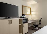 Bright studio featuring work desk with ergonomic chair, microwave, coffee maker, and TV.