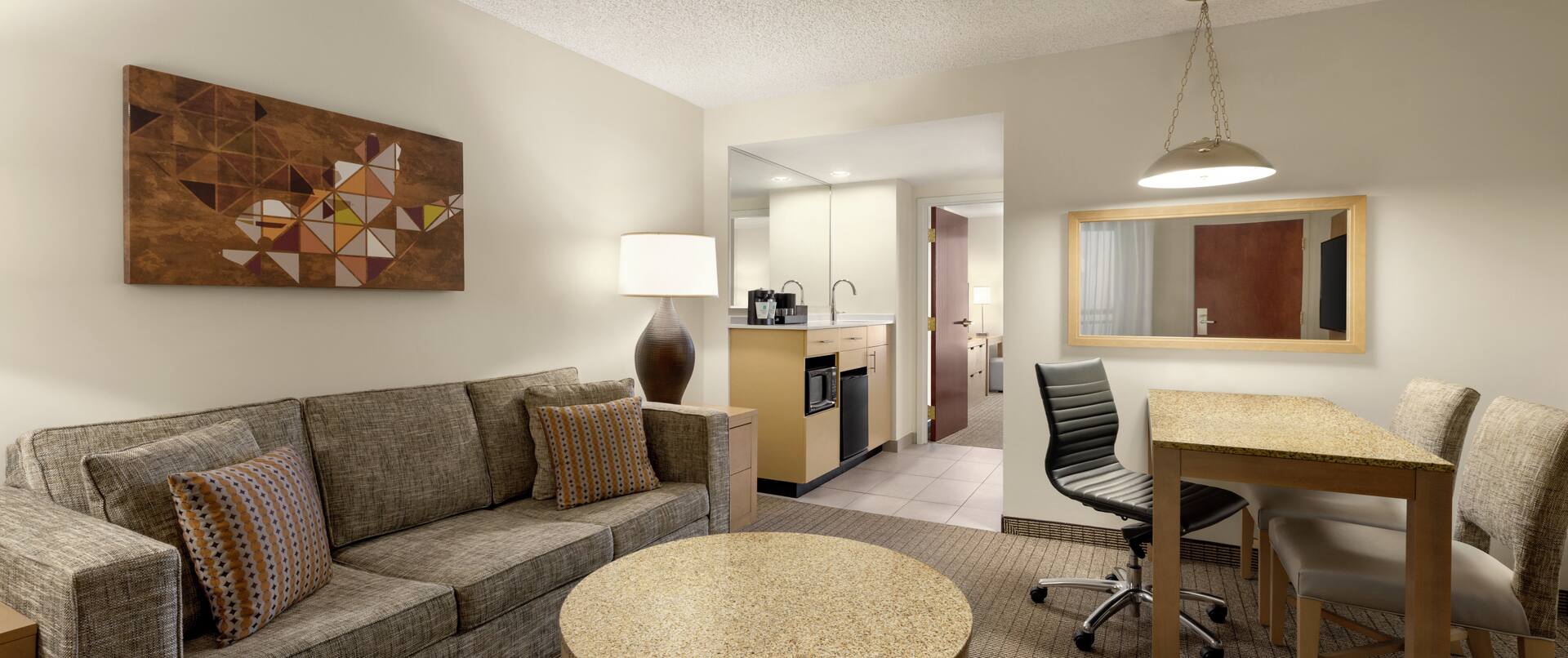 Spacious living area in suite featuring comfortable sofa, dining table, wet bar, and private bedroom.
