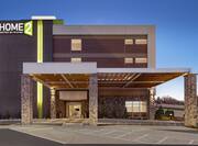Modern Home2 Suites hotel exterior featuring porte cochere, glowing lobby, and beautiful dusk sky.